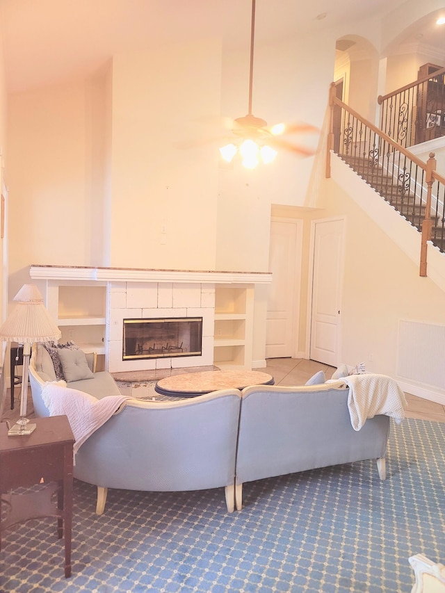 carpeted living room featuring visible vents, a ceiling fan, stairway, a high ceiling, and a fireplace