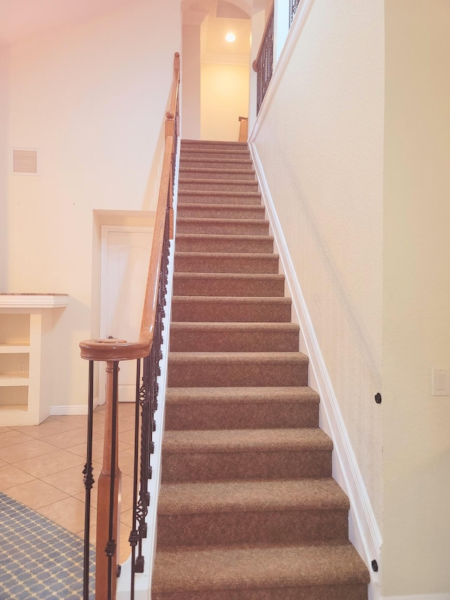 staircase featuring tile patterned floors, baseboards, visible vents, and a towering ceiling