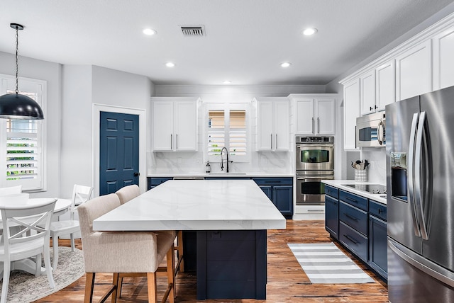 kitchen with appliances with stainless steel finishes, blue cabinets, a kitchen island, and white cabinets