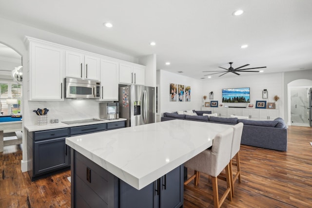 kitchen featuring a kitchen island, appliances with stainless steel finishes, dark hardwood / wood-style floors, white cabinetry, and a breakfast bar area