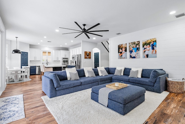 living room featuring ceiling fan, sink, light hardwood / wood-style flooring, and wood walls