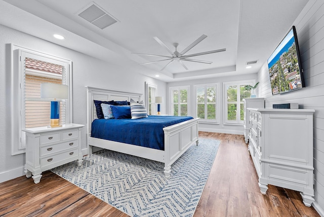 bedroom with a tray ceiling, visible vents, and wood finished floors