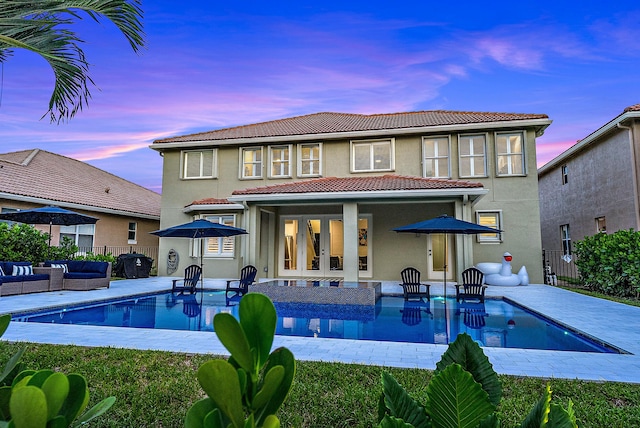 back of house at dusk featuring a patio, fence, outdoor lounge area, a tile roof, and decorative driveway