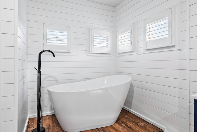 bathroom with wooden walls, wood finished floors, and a freestanding tub