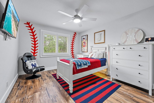 bedroom with ceiling fan, wood finished floors, baseboards, and a textured ceiling