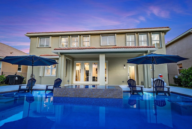 rear view of house featuring a fenced in pool, fence, stucco siding, french doors, and a tiled roof