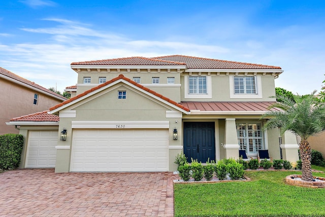 view of front of property with a front yard, a standing seam roof, an attached garage, stucco siding, and decorative driveway