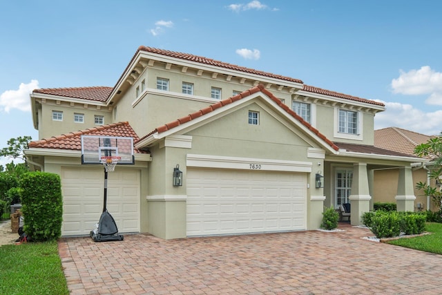 mediterranean / spanish-style home featuring stucco siding, decorative driveway, and an attached garage