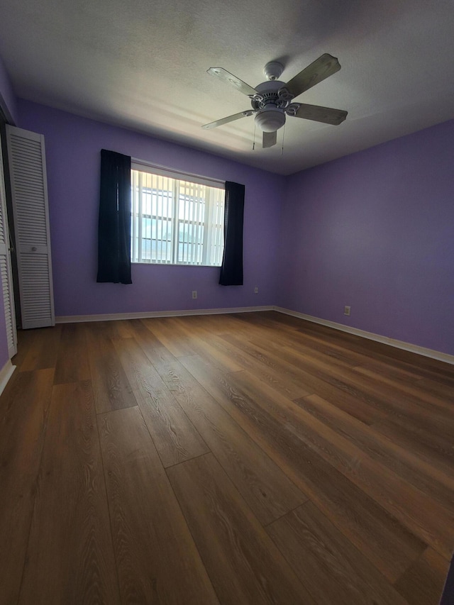 spare room with baseboards, dark wood-style floors, and a ceiling fan