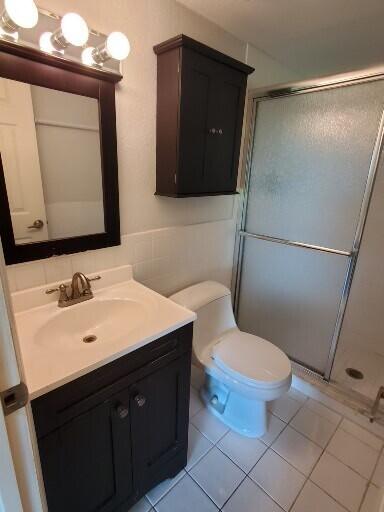 bathroom featuring tile patterned flooring, toilet, a stall shower, and vanity