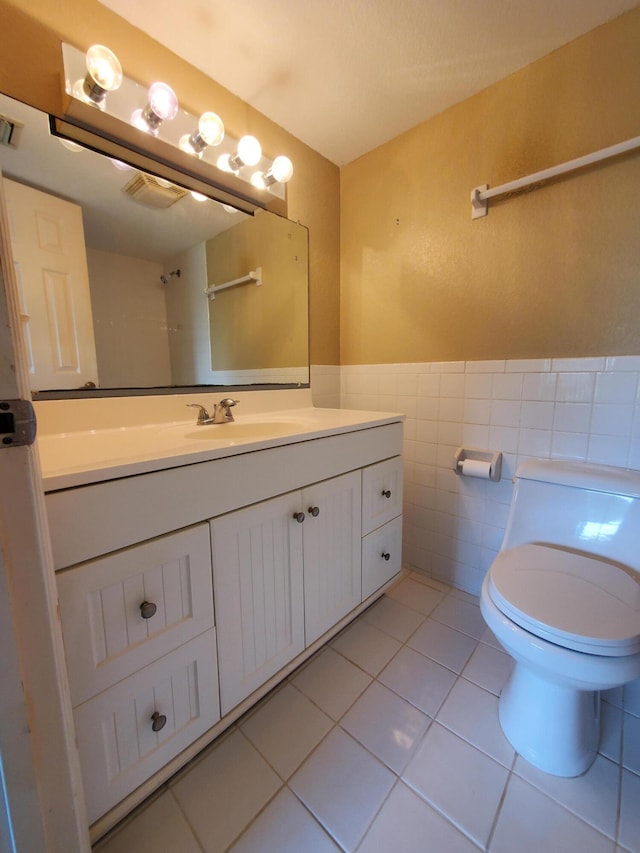 bathroom with tile patterned flooring, a wainscoted wall, toilet, vanity, and tile walls