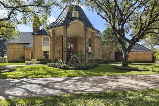 french country style house featuring a front yard, brick siding, and a chimney