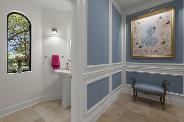 bathroom with baseboards, a healthy amount of sunlight, and a decorative wall