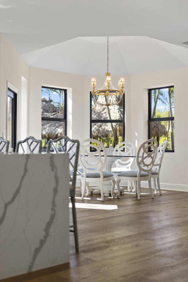 dining room featuring an inviting chandelier, lofted ceiling, wood finished floors, and baseboards