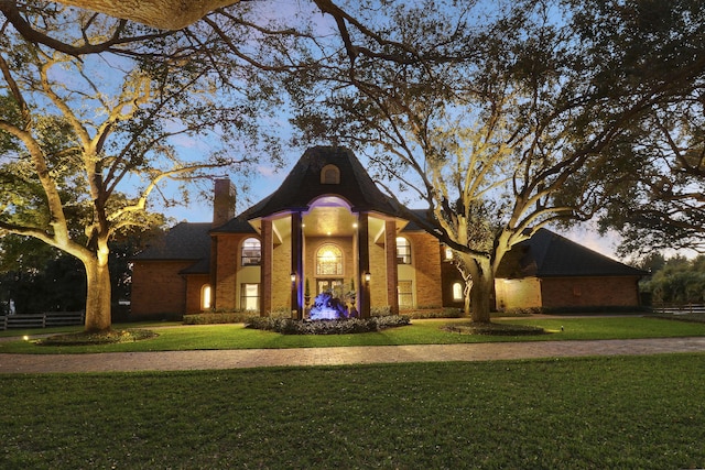 view of front facade featuring brick siding, a chimney, and a front lawn