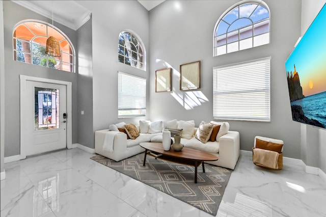 living area featuring a towering ceiling, marble finish floor, a healthy amount of sunlight, and baseboards