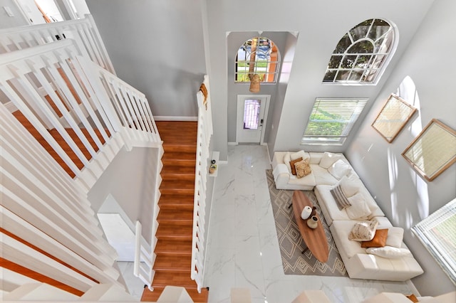 entrance foyer featuring stairs, marble finish floor, a high ceiling, and baseboards