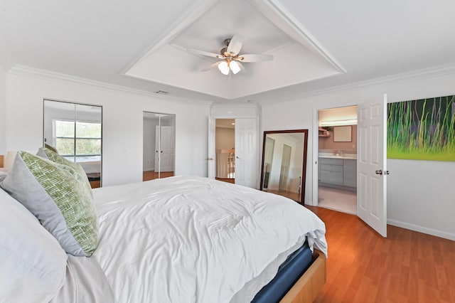 bedroom with multiple closets, ornamental molding, light hardwood / wood-style floors, and a tray ceiling