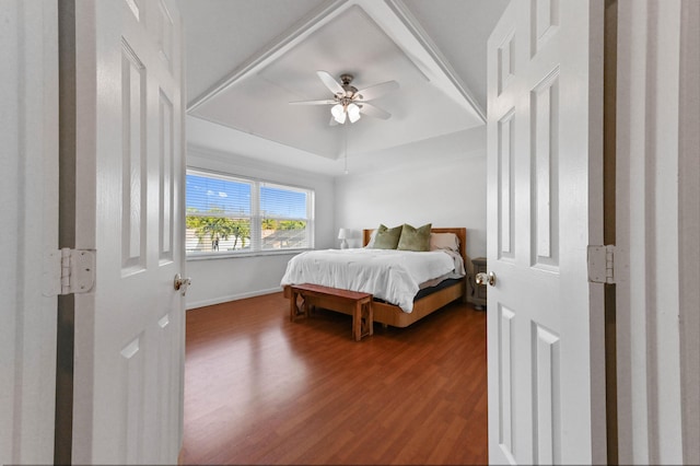 bedroom featuring a ceiling fan, a tray ceiling, baseboards, and wood finished floors