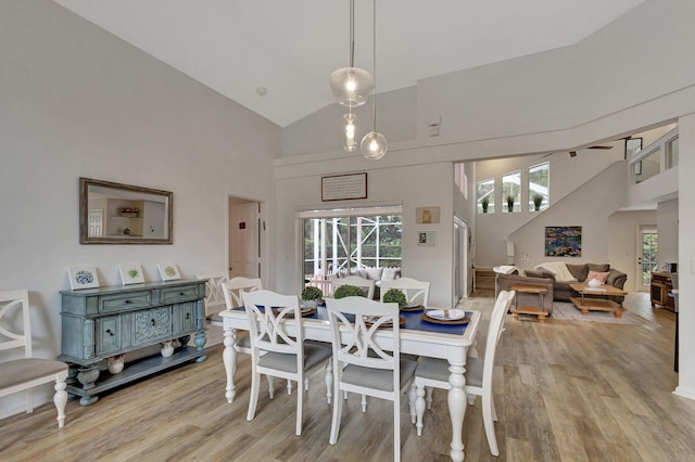 dining area with high vaulted ceiling and light hardwood / wood-style floors