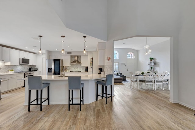 kitchen with light hardwood / wood-style flooring, a breakfast bar area, stainless steel appliances, decorative light fixtures, and wall chimney exhaust hood