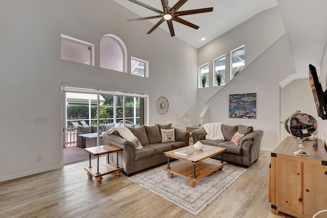 living room with ceiling fan, a towering ceiling, and light hardwood / wood-style floors