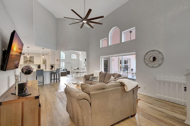 living room with a towering ceiling, plenty of natural light, light hardwood / wood-style floors, and ceiling fan