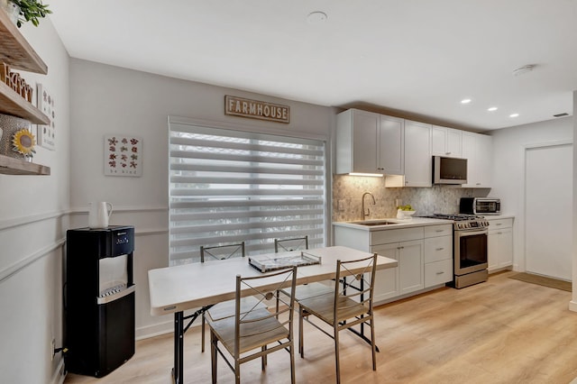 kitchen with sink, stainless steel gas stove, backsplash, white cabinets, and light wood-type flooring