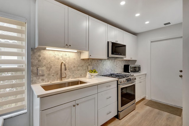 kitchen featuring sink, white cabinetry, light hardwood / wood-style flooring, appliances with stainless steel finishes, and decorative backsplash