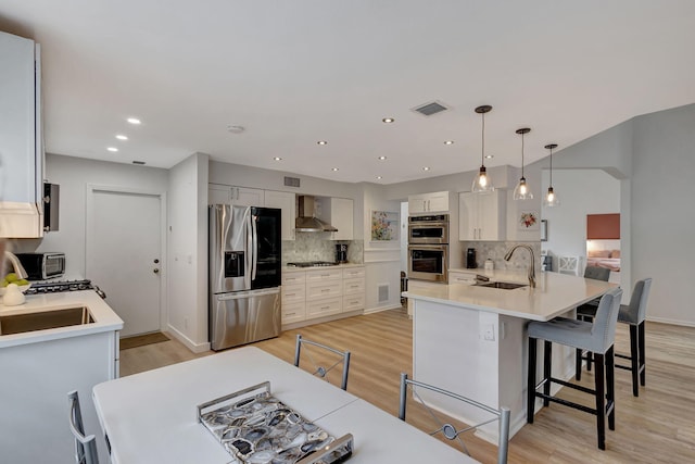 kitchen with wall chimney exhaust hood, sink, white cabinetry, decorative light fixtures, and stainless steel appliances