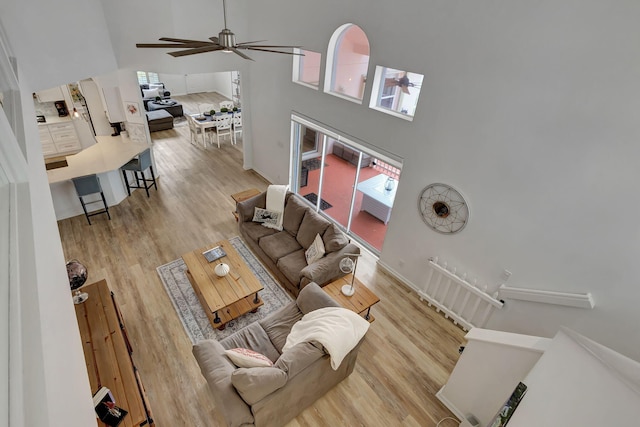 living room featuring a towering ceiling, ceiling fan, and light wood-type flooring