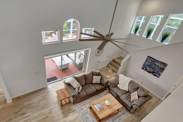 living room with a towering ceiling, ceiling fan, and light hardwood / wood-style flooring