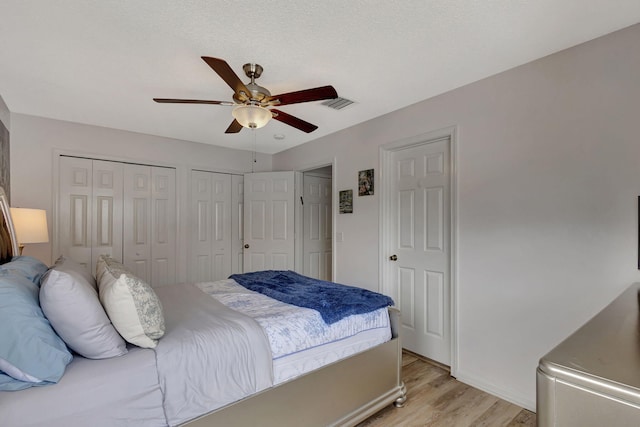 bedroom featuring ceiling fan, two closets, and light wood-type flooring