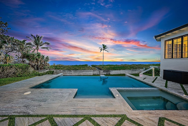 pool at dusk with a deck with water view and an in ground hot tub