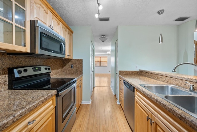 kitchen featuring sink, hanging light fixtures, a textured ceiling, stainless steel appliances, and light hardwood / wood-style floors