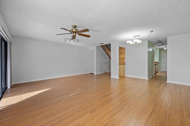 unfurnished living room featuring ceiling fan with notable chandelier, a textured ceiling, and light wood-type flooring