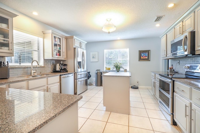 kitchen with sink, appliances with stainless steel finishes, a textured ceiling, light tile patterned flooring, and decorative backsplash