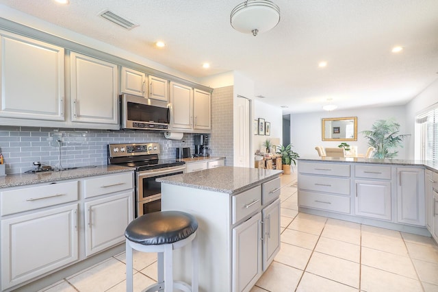 kitchen featuring light tile patterned floors, decorative backsplash, a kitchen island, and appliances with stainless steel finishes