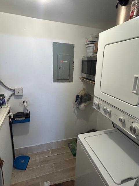 laundry room featuring stacked washer and dryer, dark wood-type flooring, and electric panel