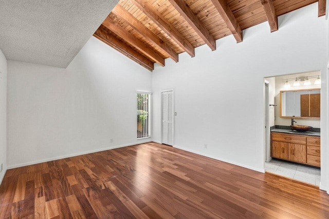 unfurnished living room featuring wooden ceiling, beamed ceiling, light wood finished floors, and a sink