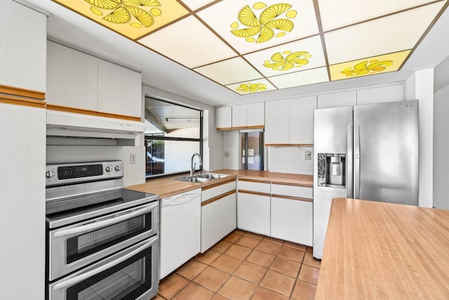 kitchen with a sink, under cabinet range hood, appliances with stainless steel finishes, white cabinets, and butcher block counters