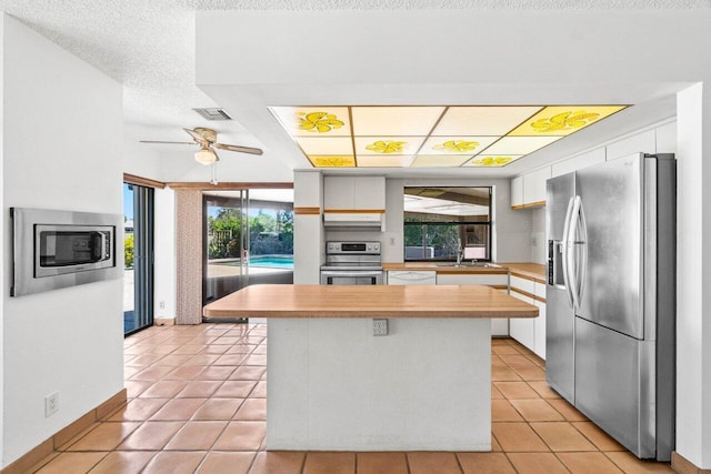 kitchen with under cabinet range hood, a kitchen island, stainless steel appliances, white cabinets, and light countertops