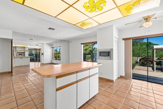 kitchen with light tile patterned floors, stainless steel microwave, a ceiling fan, and white cabinetry