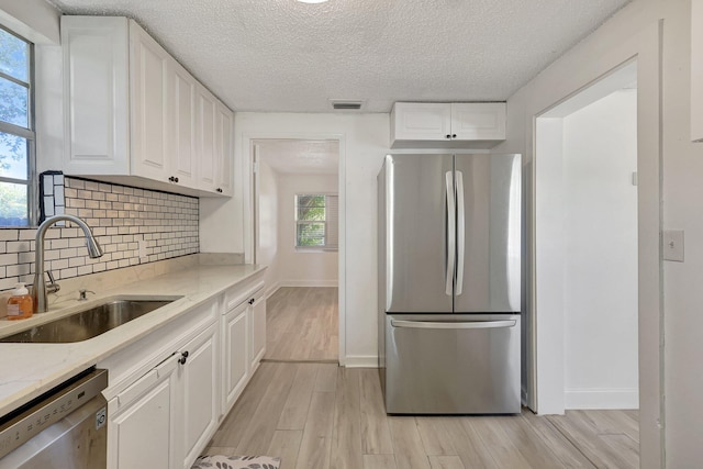 kitchen with appliances with stainless steel finishes, white cabinetry, sink, light stone countertops, and light hardwood / wood-style flooring