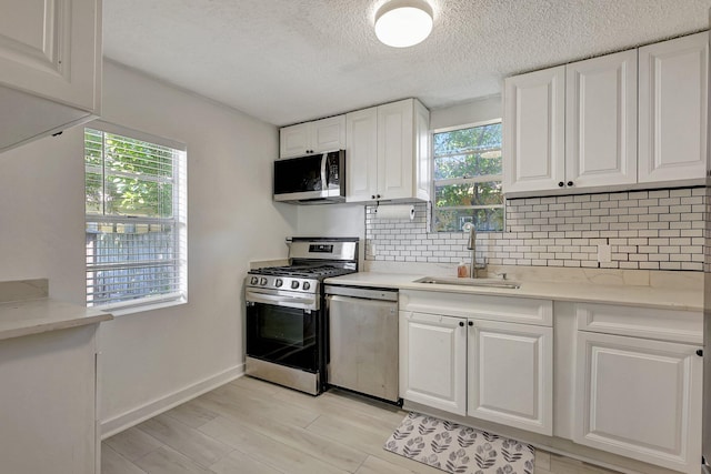 kitchen with stainless steel appliances, white cabinetry, sink, and a wealth of natural light