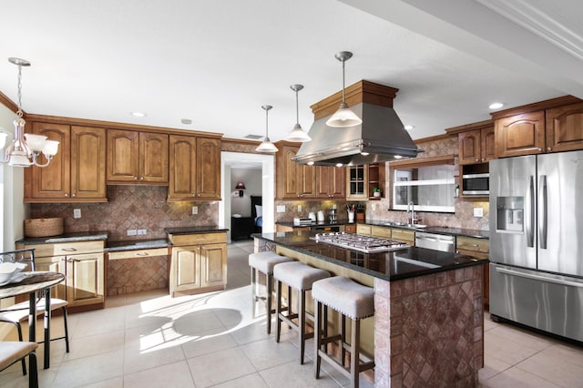 kitchen with island exhaust hood, appliances with stainless steel finishes, decorative light fixtures, and a center island