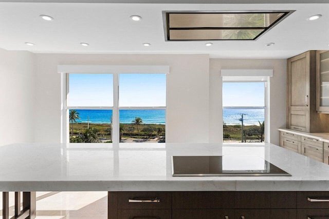 kitchen with glass insert cabinets, a water view, light stone countertops, black electric stovetop, and recessed lighting