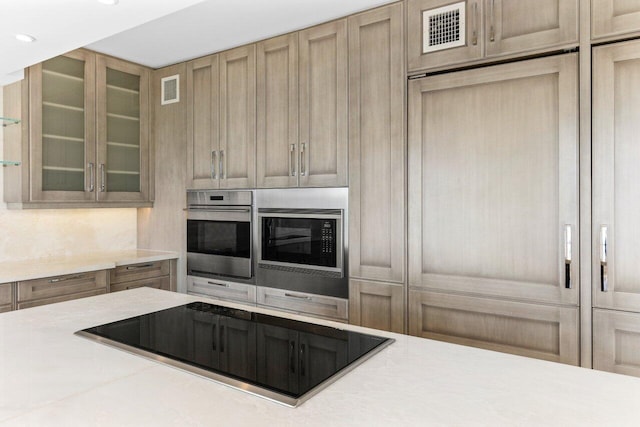 kitchen featuring light countertops, visible vents, glass insert cabinets, stainless steel oven, and black electric cooktop