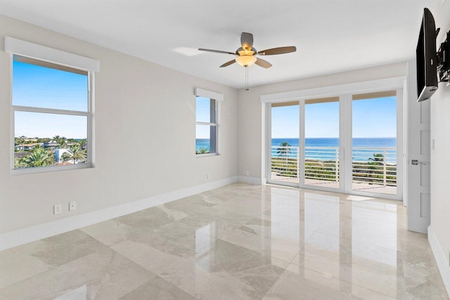 unfurnished room with marble finish floor, a ceiling fan, a wealth of natural light, and baseboards