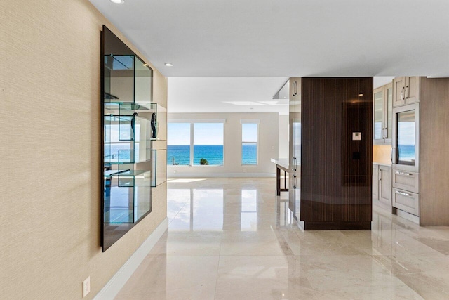 hallway with a textured wall, marble finish floor, a water view, and baseboards